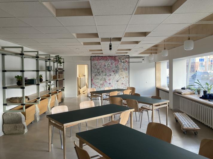 Picture of the Circular Economy Hub, with second-hand and repurposed tables and chairs, a shelving area, plants, and a piece of art made of communication wires in the centre. 