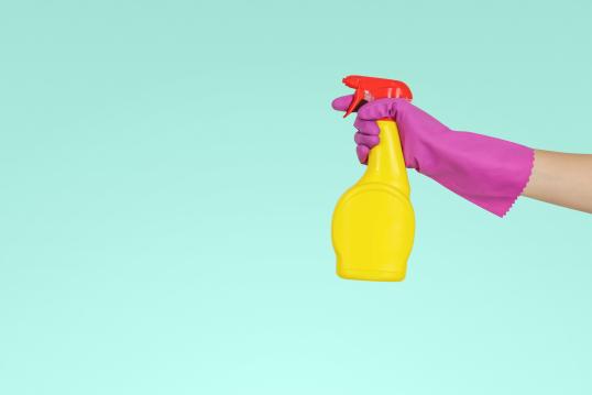 Image of one arm with a pink glove holding the yellow spray to clean up
