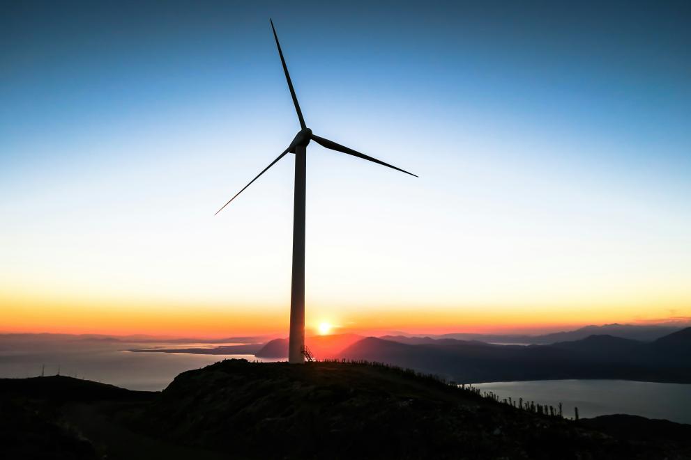 Image of a windmill, on a hill with a sunset in the background.