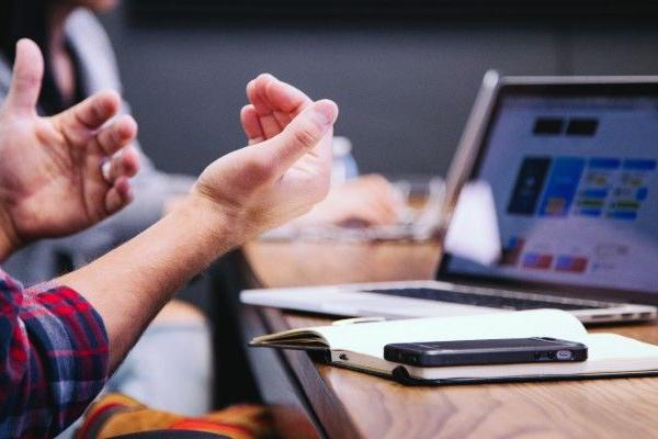 Hands are in motion, as if talking to someone, in front of a laptop during a meeting