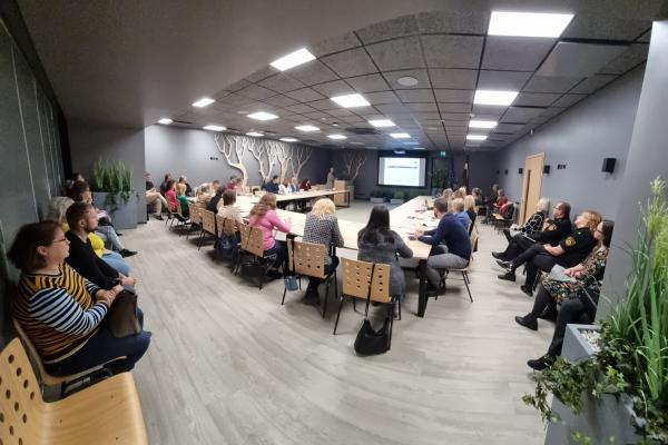 Picture from the Latvian Seminar. People sat around a U shape table, looking at a white board in the middle.