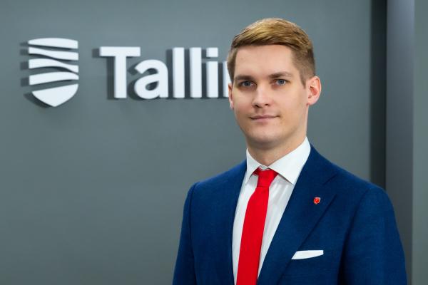 Image of a man in a blue suit, red tie and white shirt, with a sign with the word Tallinn on the back.