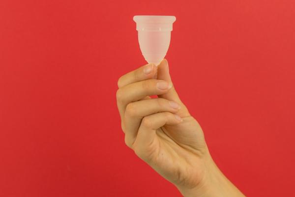 Red background image with a hand holding a transparent menstrual cup. 